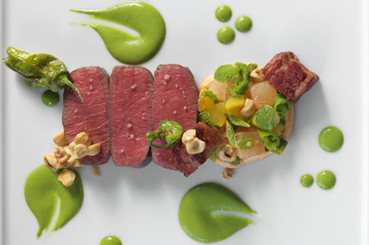 4 pieces of rare lamb with 3 circles of green sauce on white plate