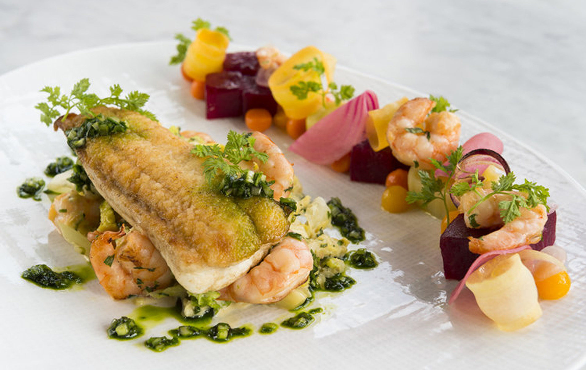 fried fish on top of shrimp and dots of green sauce surrounded by beets and vegetables