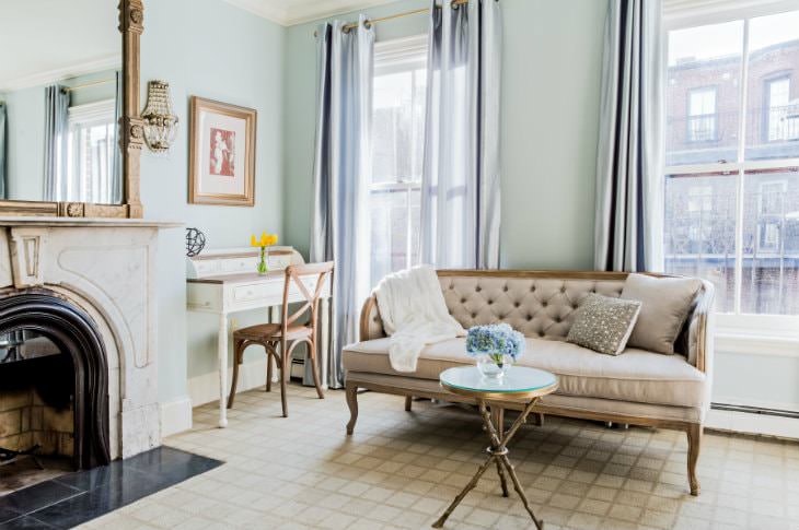 Light blue room with two large windows, fireplace, large mirror, secretary desk, and beige settee