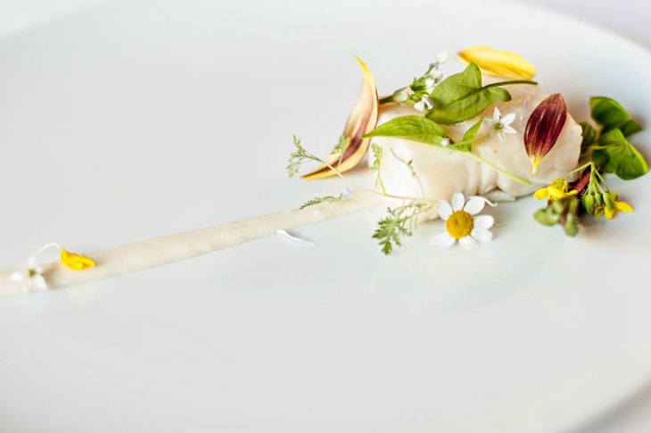 Artistic gourmet dish sprinkled with small delicate white, green and yellow flowers and leaves on a white plate