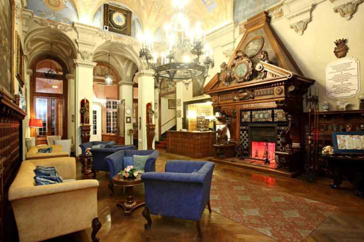 Elegant Italian hotel lobby with murals, arched doorways, elaborate chandelier, wood floors, fireplace and blue and gold seating