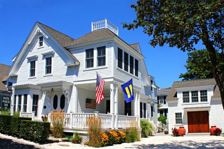 White Victorian inn surrounded by shrubs with a few trees and blue skies in the background