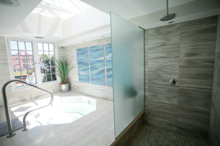 Modern tiled room with jacuzzi sunlit by large skylight next to a walk-in shower with rain shower head