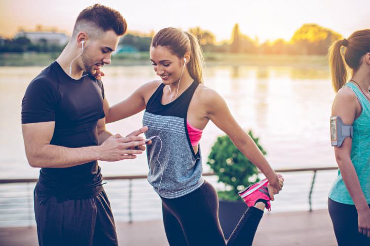 Man and woman in black workout clothes wearing ear buds getting ready to run alongside a body of water