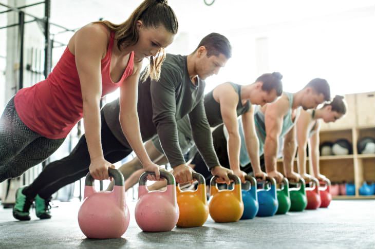 Five men and women doing push-ups on pink, orange, blue, green and red medicine balls