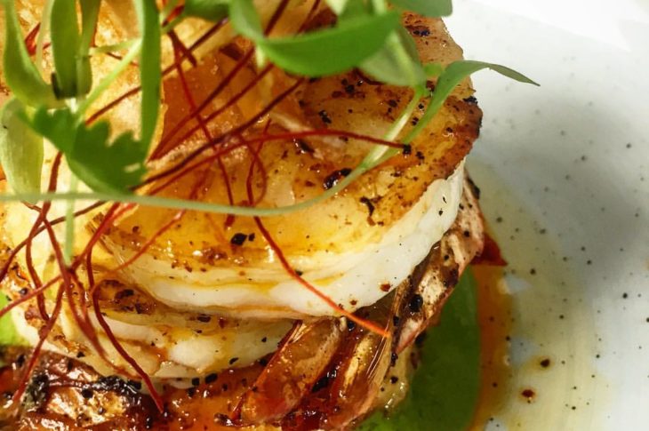 up close photo of shrimp stacked with green sprig on top of green sauce