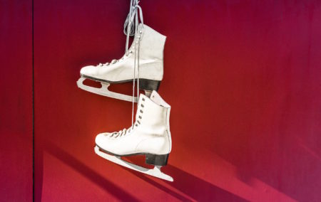 two white ice skates hanging on a red background