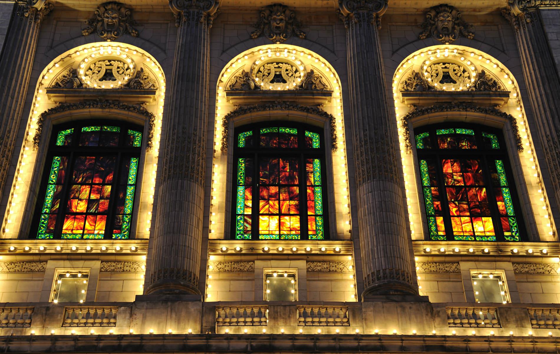 Ornately carved stone building lit up at night with tall arched windows, Grecian columns, stained glass