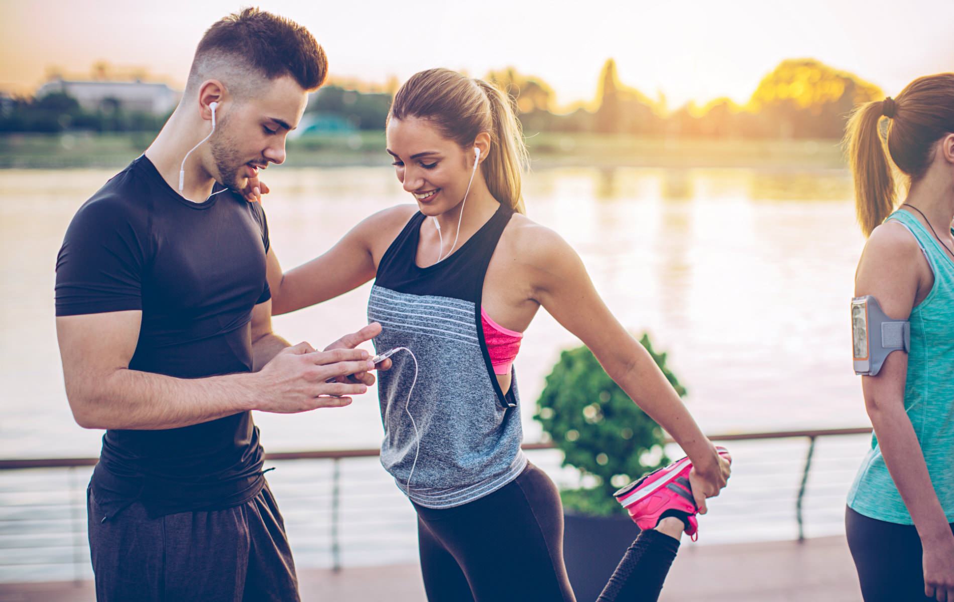 Man and woman in black workout clothes wearing ear buds getting ready to run alongside a body of water