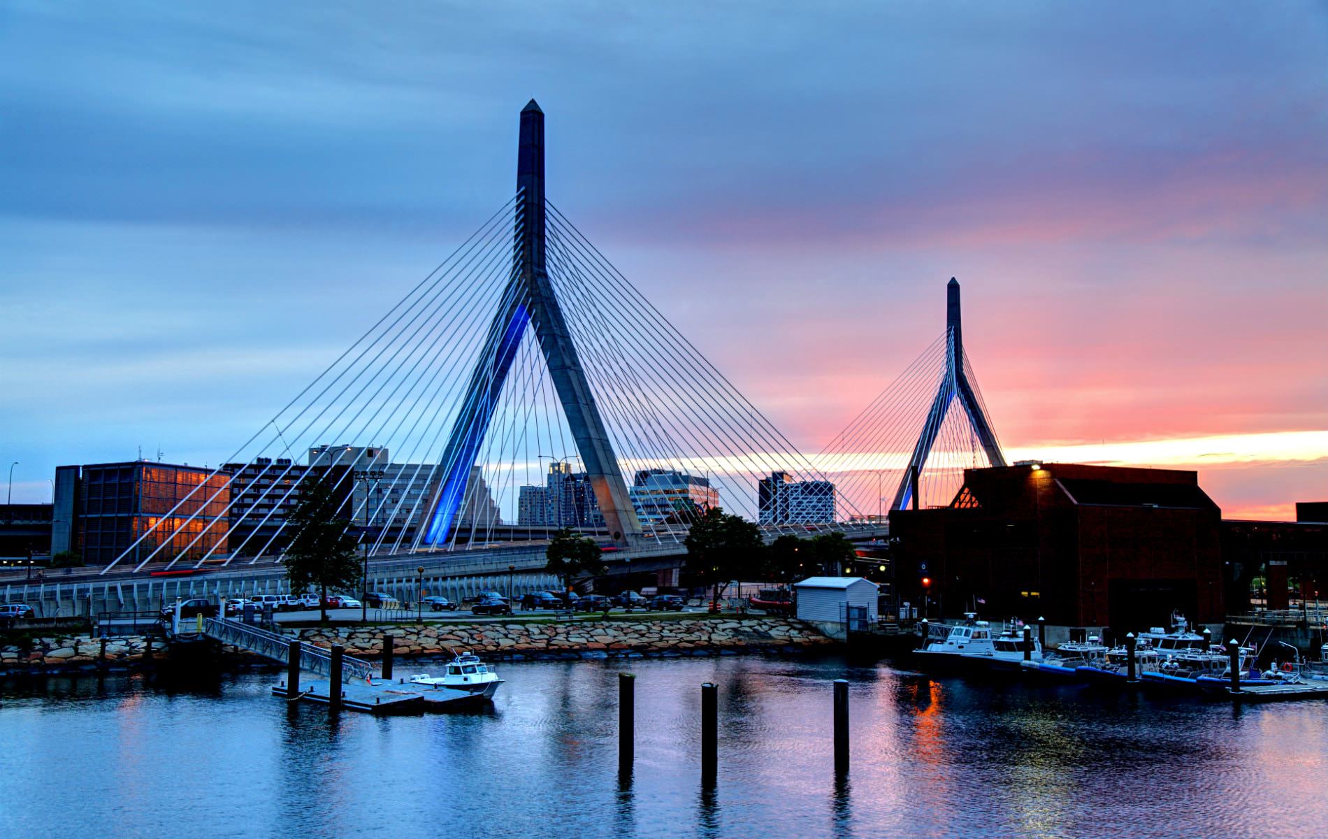 Suspension cable bridge near a harbor at dusk with blue, pink and yellow skies