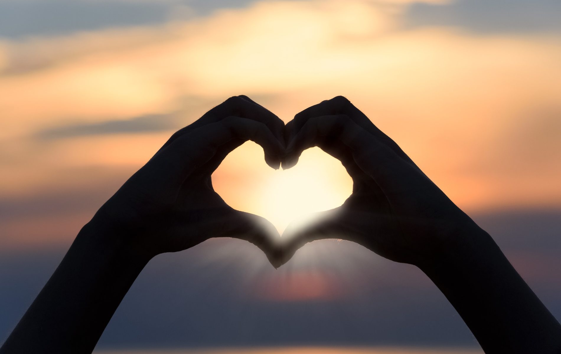two hands in the shape of a heart with a sunset