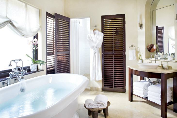 Beige bathroom with tile floor, freestanding white tub, wood vanity with vessel link, white towels and white robe