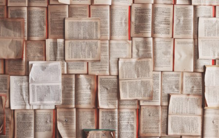 a pile of books all open with white pages and black text overlapping the entire surface