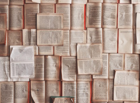 a pile of books all open with white pages and black text overlapping the entire surface
