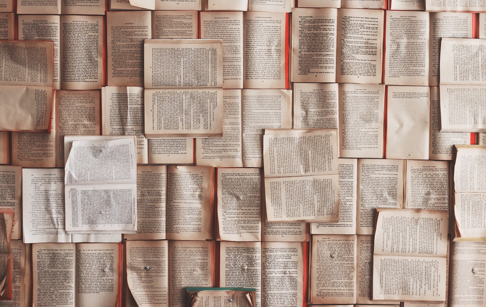 a pile of books all open with white pages and black text overlapping the entire surface