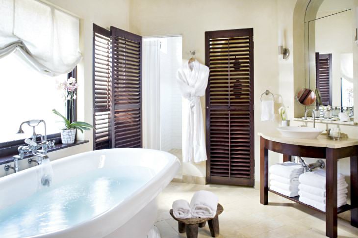 White bathroom with marble floor, freestanding white tub, wood vanity with vessel link, white towels and white robe