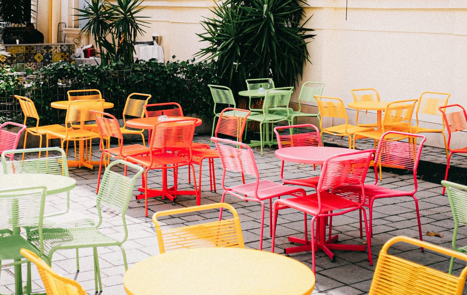 clusters of yellow, red, orange and green table and chairs outside on grey pavers