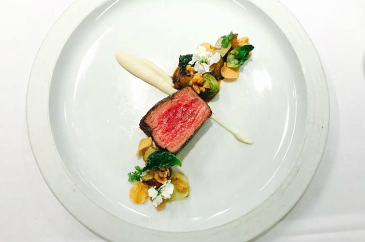 Artistic gourmet dish of seared meat sprinkled with green and white flowers on a white plate