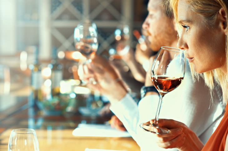 Woman sniffing a glass of red wine at a bar alongside several other people