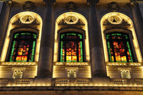 Ornately carved stone building lit up at night with tall arched windows, Grecian columns, and stained glass