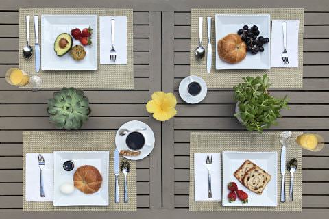 Gray patio table set for four with different breakfast plates of strawberries, avocado, croissants, blueberries, toast, juice, and coffee
