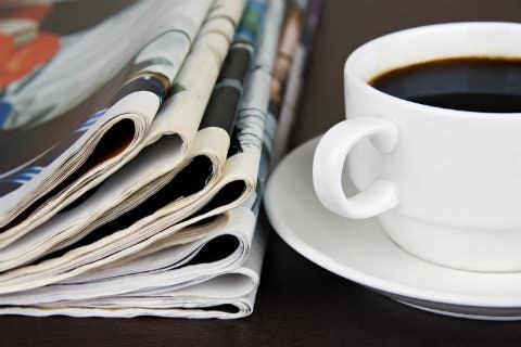 Stack of folded newspapers next to a white cup and saucer filled with coffee