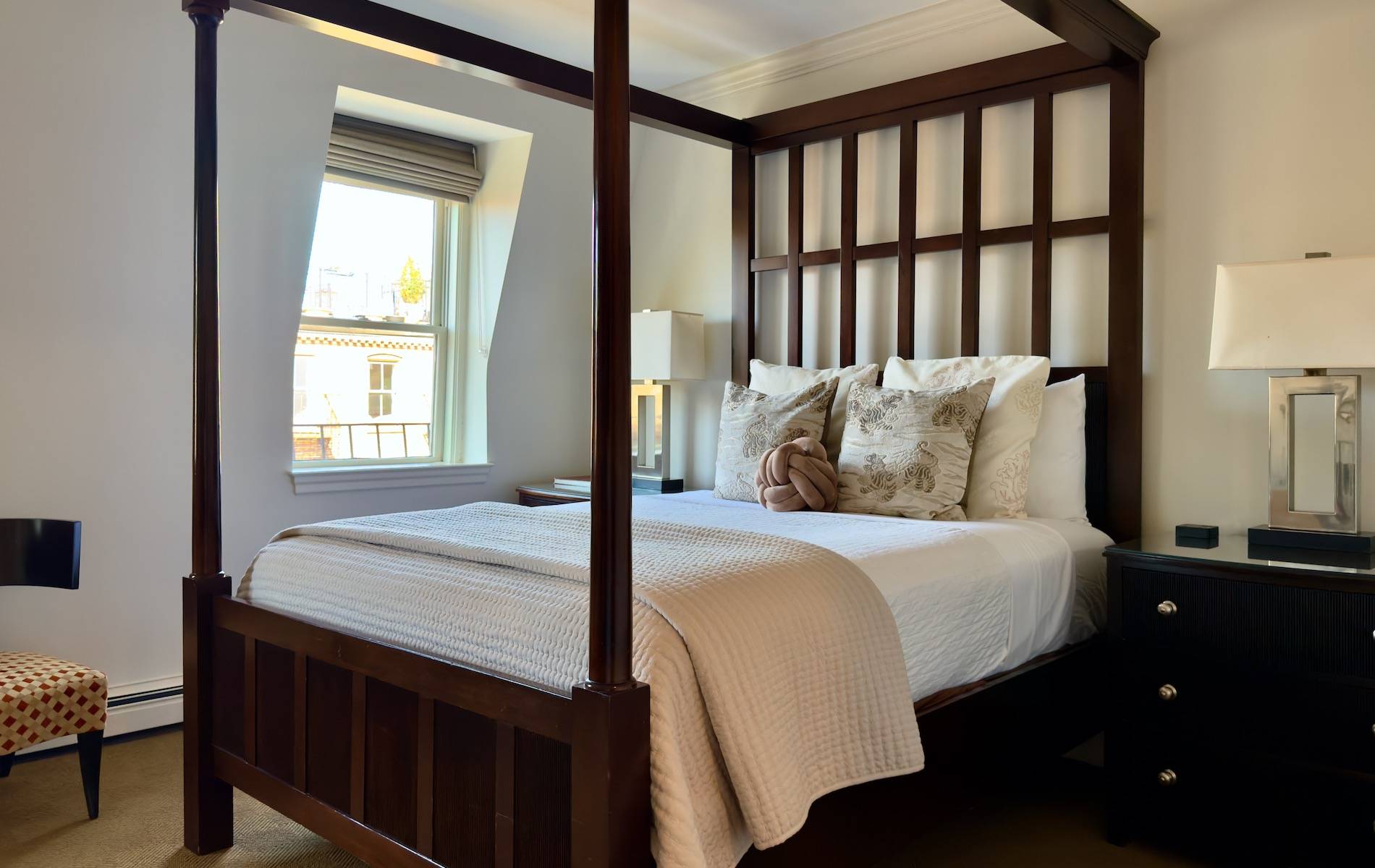 Romantic guest room with 4 poster mahogany bed, white walls and tone on tone decorative pillows. 