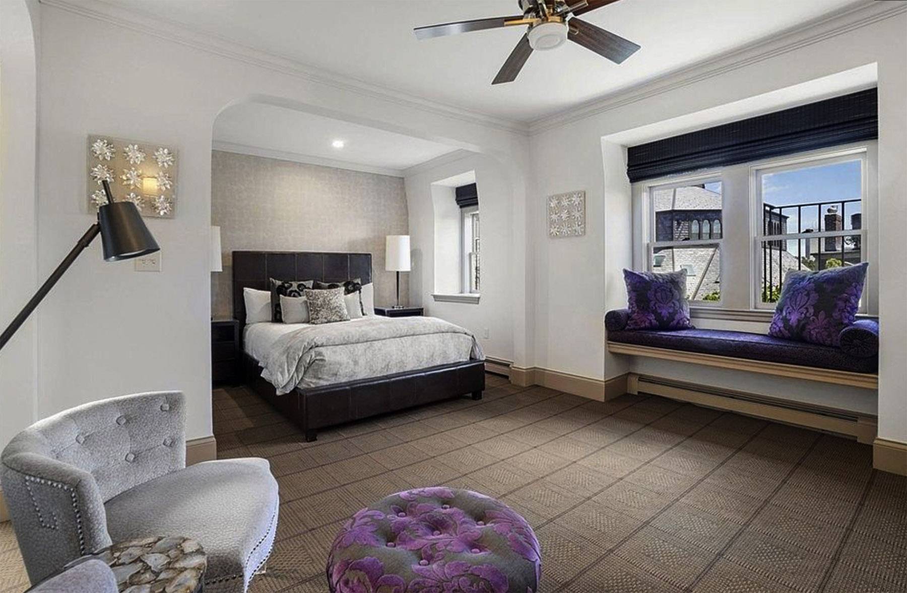 Bed with brown headboard, purple pillows and silver duvet - two side lamps and silver wallpaper.