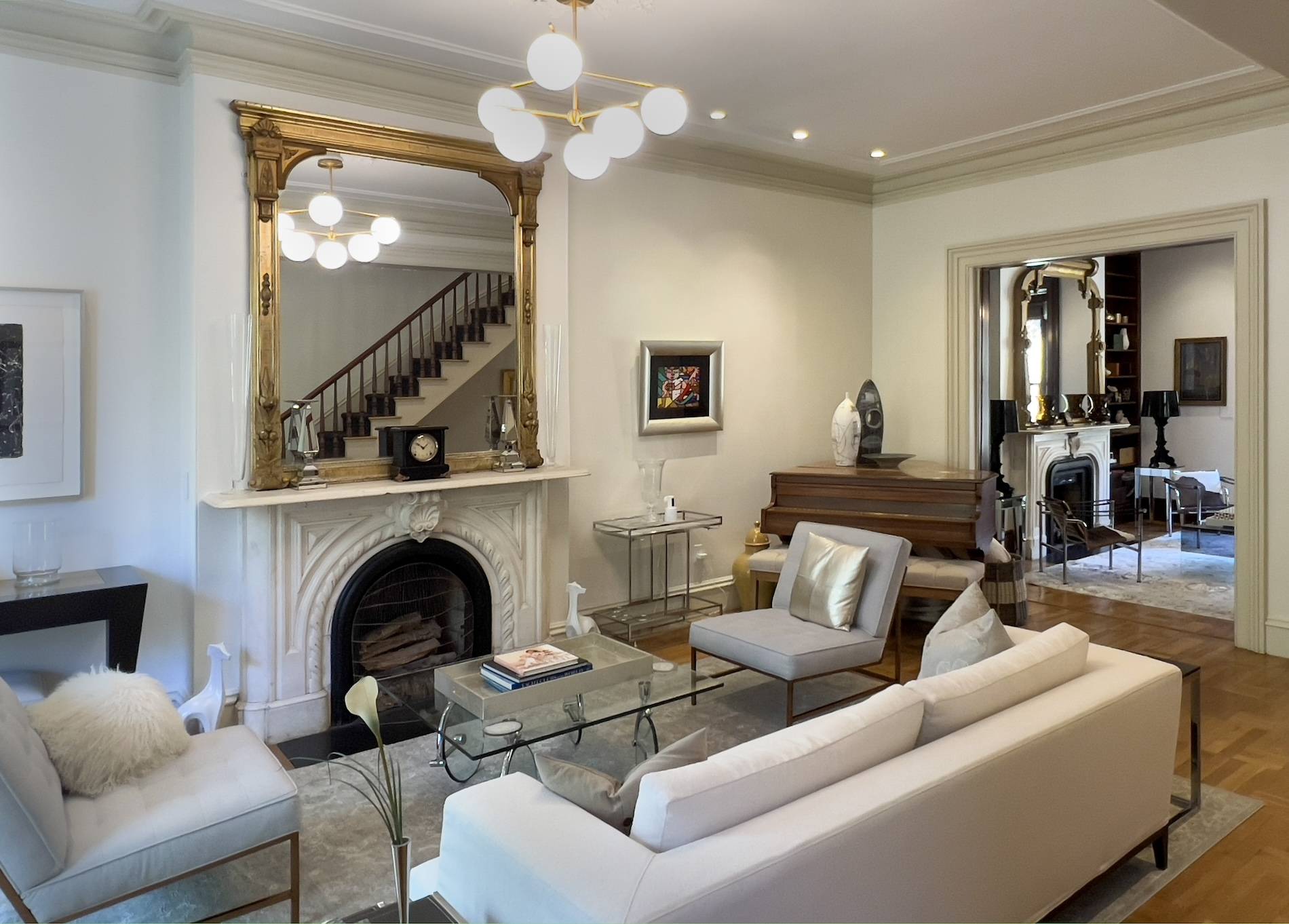 White Victorian parlor with white and grey furniture, gold mirror over white marble mantle and oak floors.