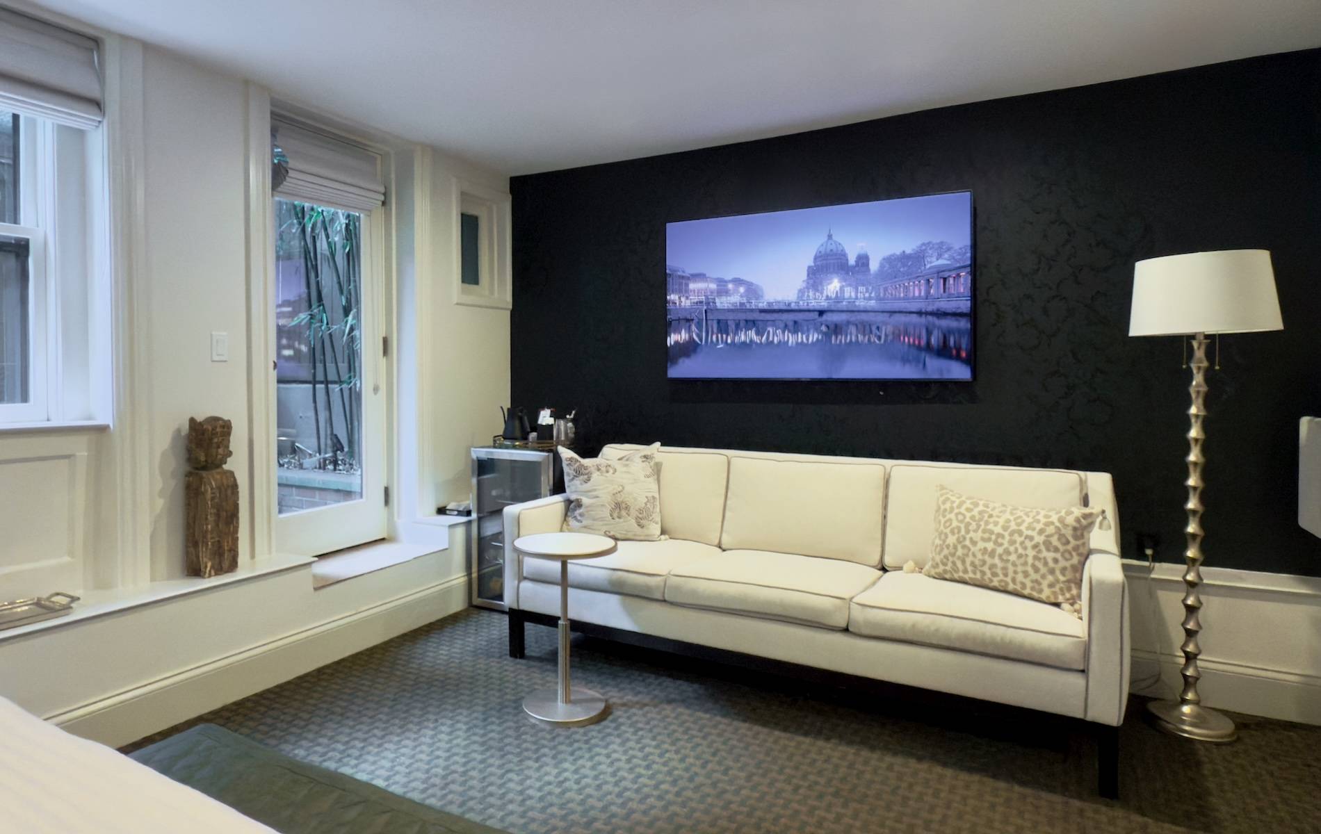 Bedroom with white walls, black wallpaper behind a white sofa. Dark green carpet and door onto garden.