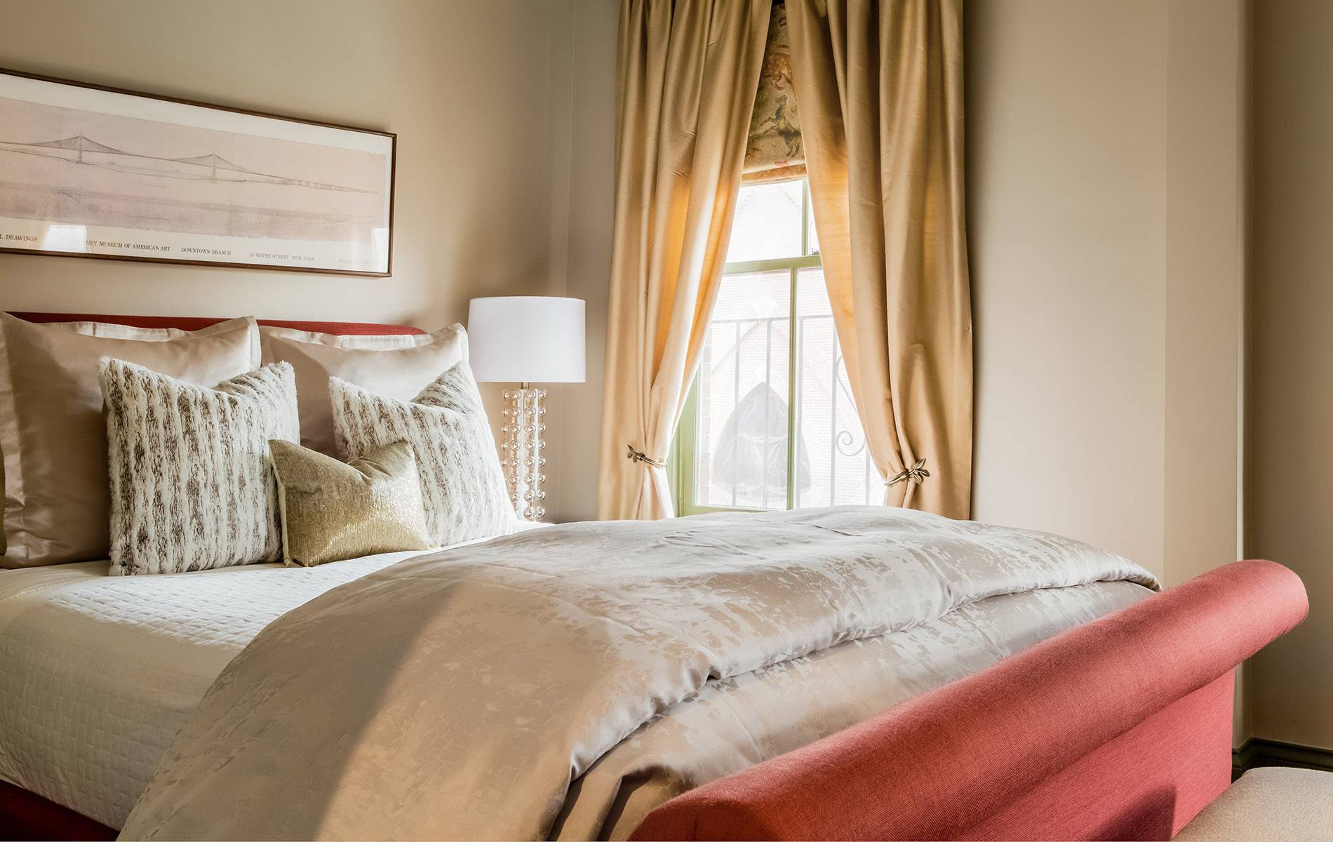 Bedroom with red upholstery, gold curtains, glass lamps and shimmery duvet.