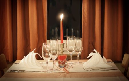 White table cloth table set for two with a red candle and red curtains