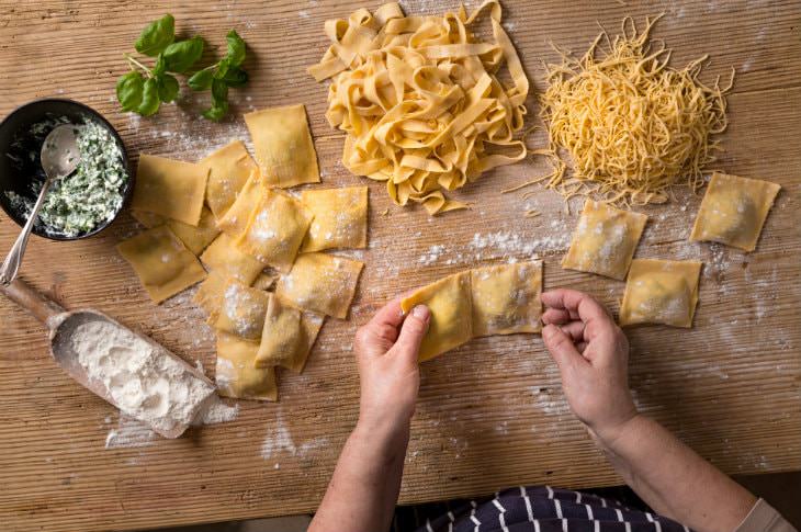 Woman's hands making homemade pasta and noodles on a wooden table dusted with white flour