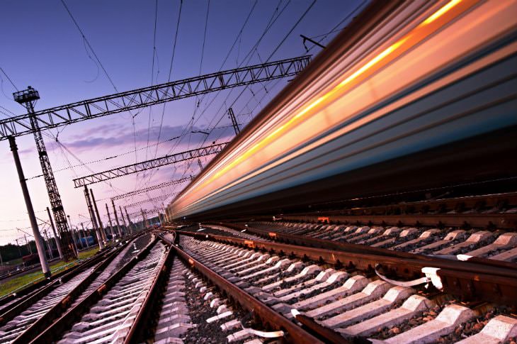 Ground level view of extensive rail system with blurred train racing by amidst purple and pink skies