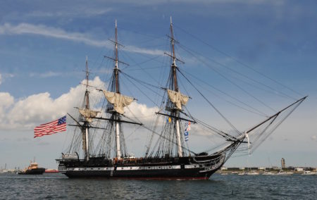 historic 3 mast ship on water with 3 sails and one american flag to the left