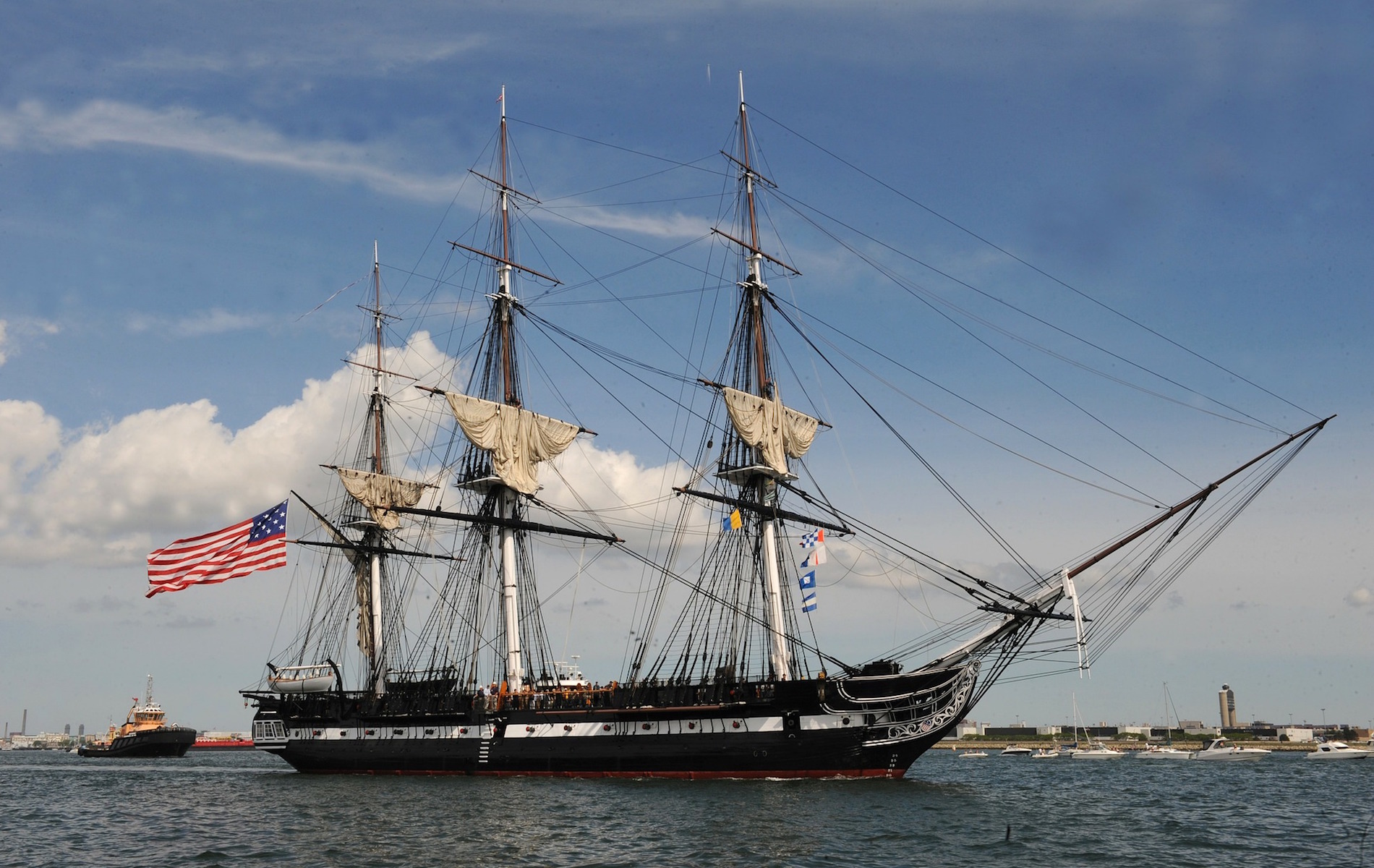 historic 3 mast ship on water with 3 sails and one american flag to the left